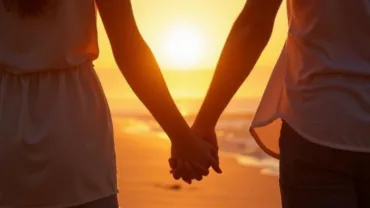 Couple holding hands walking on a beach at sunset