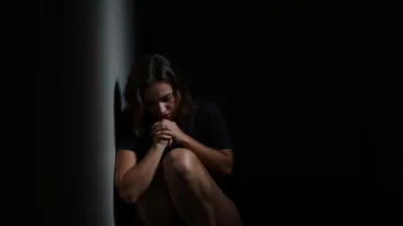 Woman huddled in fear, surrounded by shadows