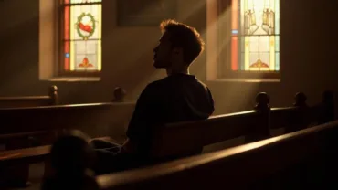 Person sitting alone in a church pew, deep in thought.